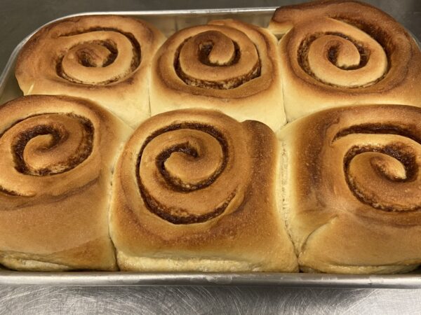 A set of six golden brown Caramel Rolls, freshly baked and arranged in two rows of three.