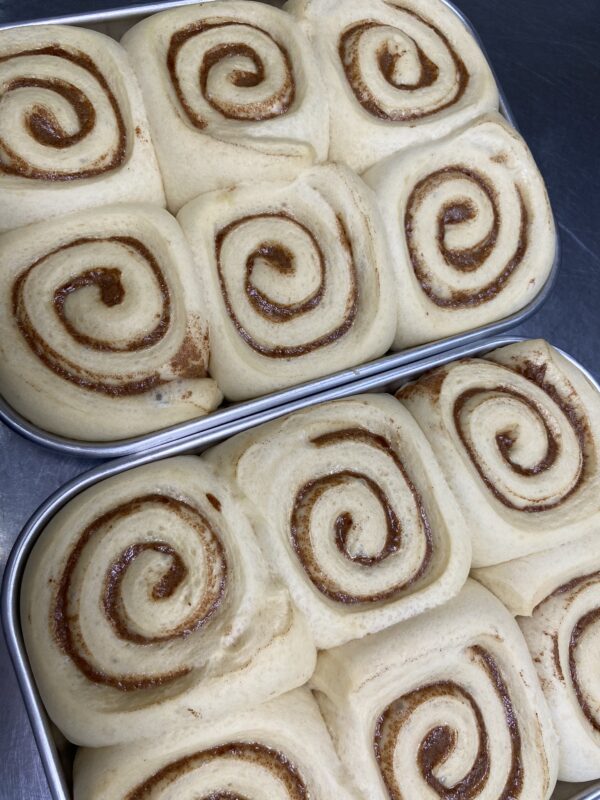 Two trays of unbaked caramel rolls, arranged closely with visible spiral patterns.