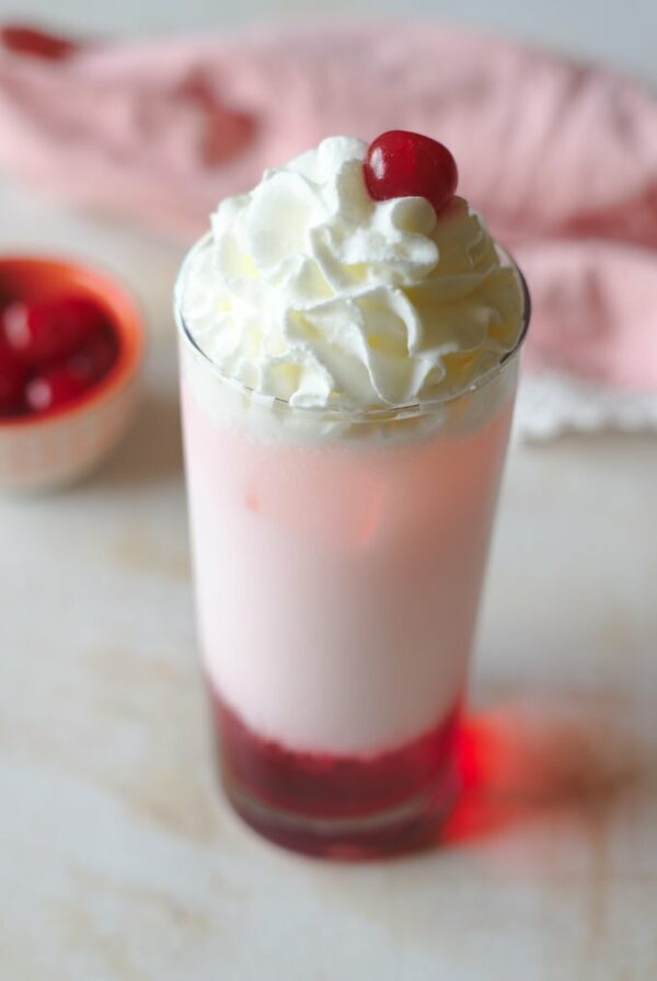 A glass of white liquid with whipped cream and cherries on top.
