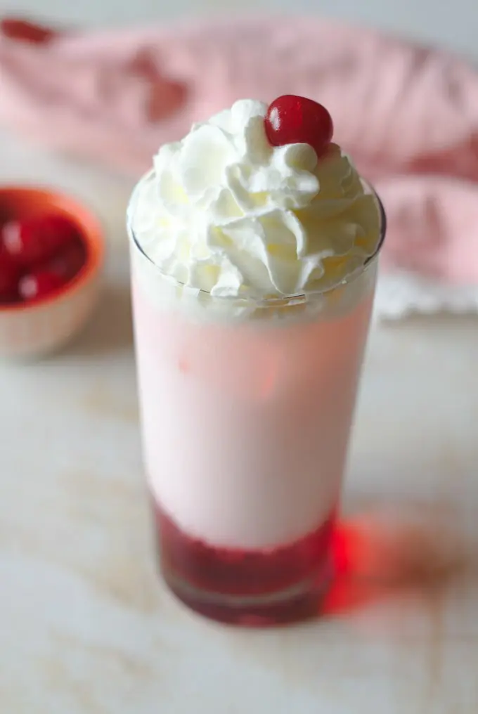 A glass of white liquid with whipped cream and cherries on top.
