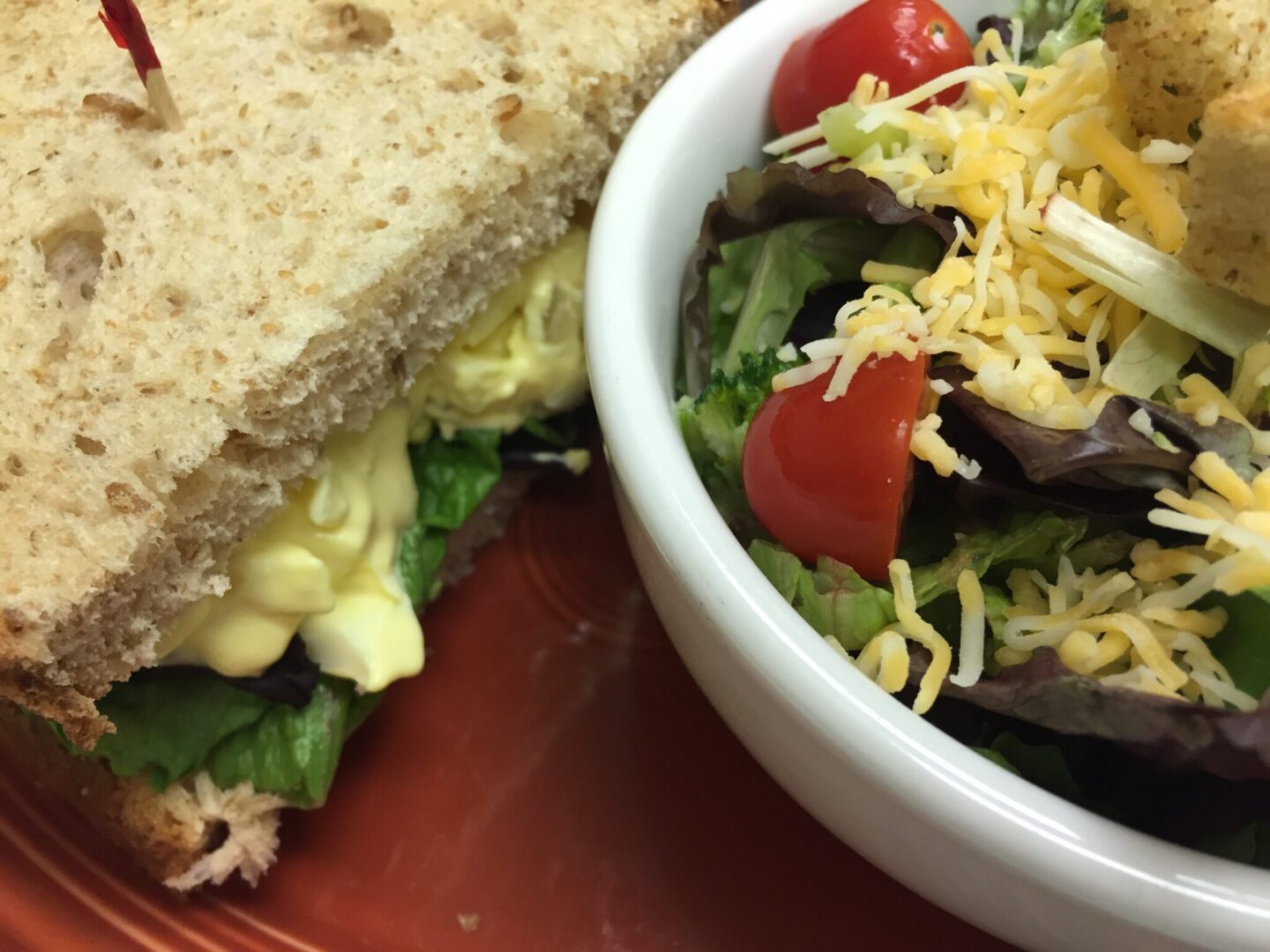 A bowl of salad and sandwich on the side.