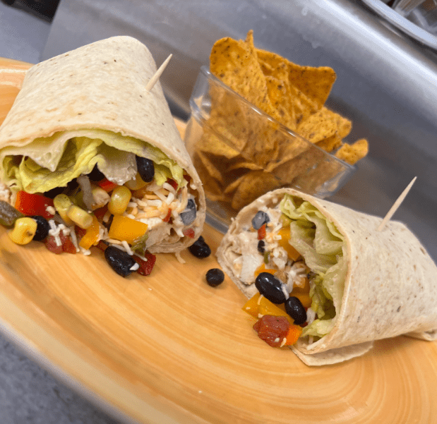 A plate with two burritos and some chips on it