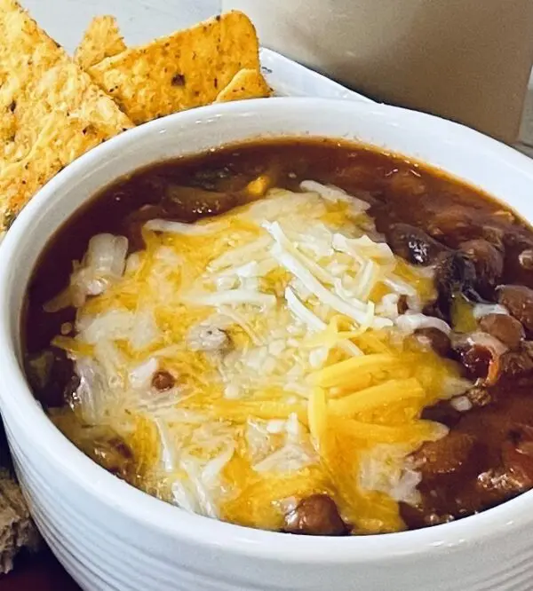 A bowl of chili with cheese and tortilla chips.