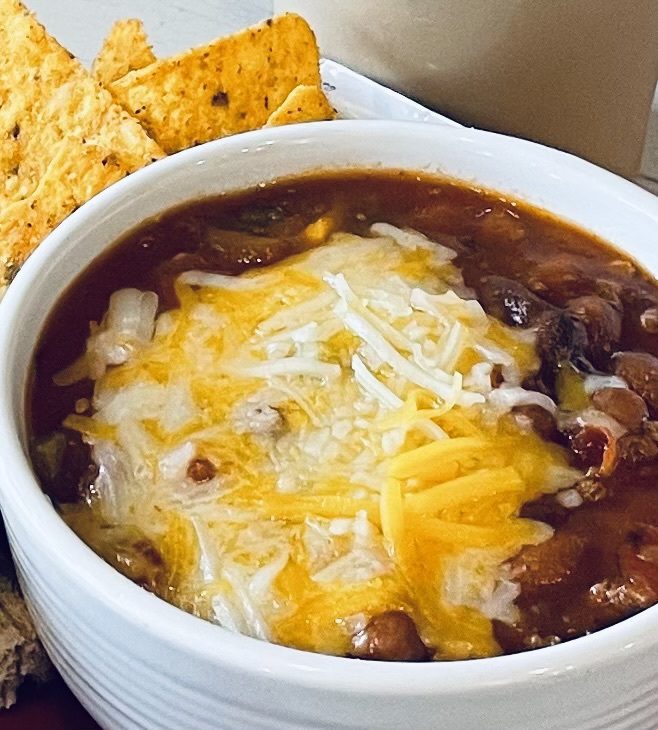 A bowl of chili with cheese and tortilla chips.
