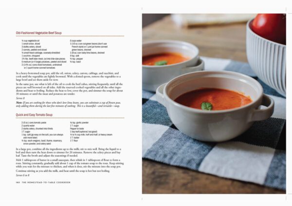 Open the Homestead To Table Cookbook featuring recipes for Old-Fashioned Vegetable Beef Soup and Quick and Easy Tomato Soup, next to two bowls of tomato soup on a striped cloth.