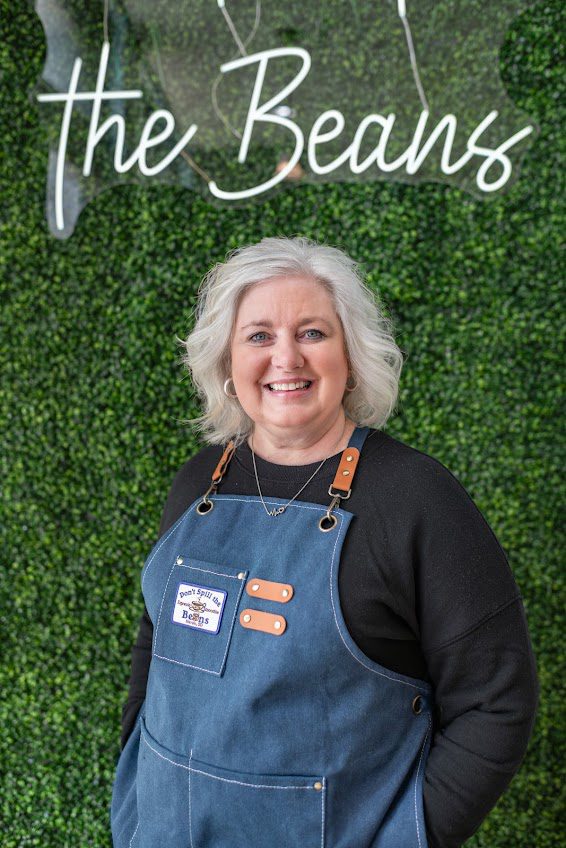 A woman standing in front of a wall with the beans sign.