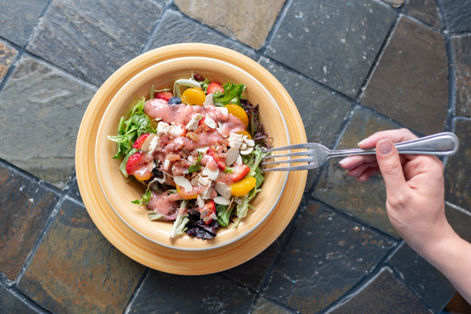 A person holding a fork over a bowl of salad.