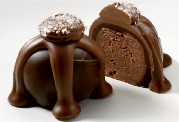 Two chocolate truffles with a glossy coating, topped with sugar crystals. One is whole; the other is cut in half to reveal a rich, creamy interior.