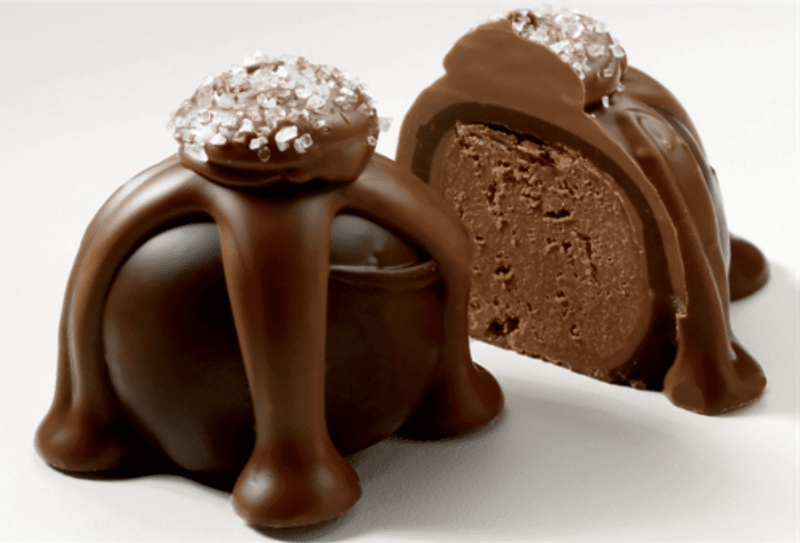 Two chocolate truffles with a glossy coating, topped with sugar crystals. One is whole; the other is cut in half to reveal a rich, creamy interior.