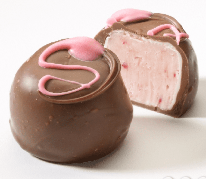 A chocolate-covered truffle is cut open, revealing a pink creamy filling. The truffle is topped with pink decorative icing.