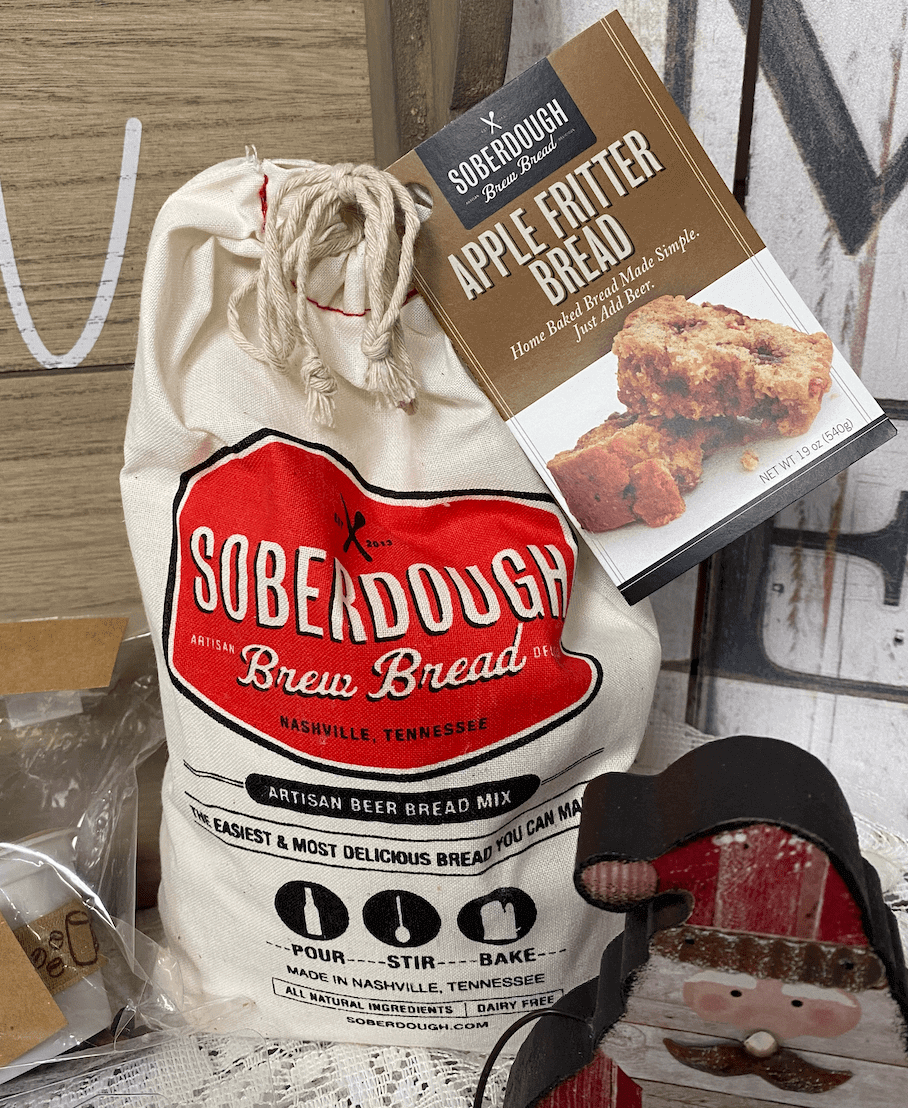 Sack of Soberdough Brew Bread Mix with a box of Apple Fritter Bread mix beside it, displayed on a wooden surface.