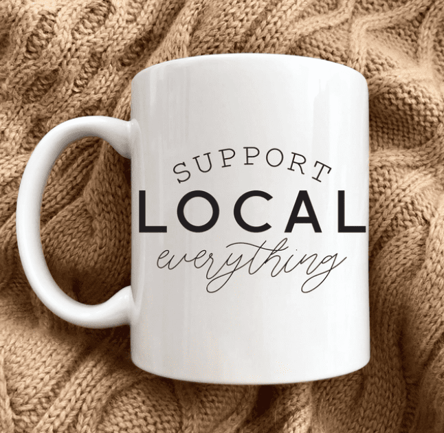 White mug with the text "Support Local Everything" on a textured, knitted fabric background.