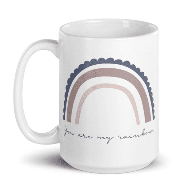 White mug with a minimalist rainbow design in muted colors and the text "You are my rainbow" in cursive.
