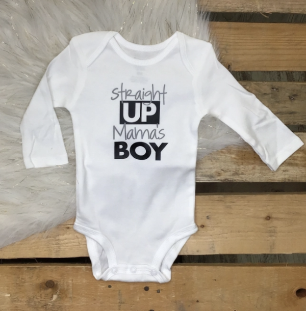 White baby onesie with the text "Straight Up Mama's Boy" printed in black on a wooden surface.