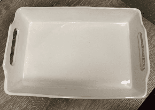 A large white ceramic baker dish with handles on a wooden surface.