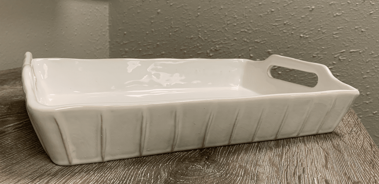 A white ceramic baking dish with a handle sits on a wooden surface.