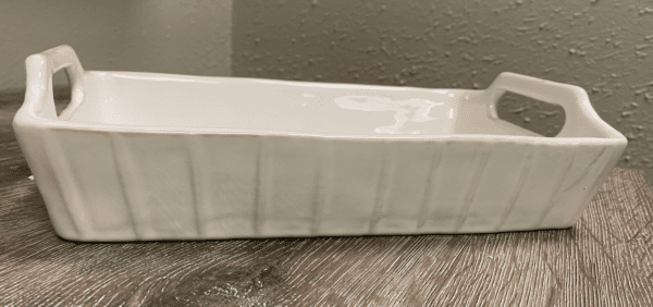 White rectangular ceramic baking dish with handles on a wooden surface against a textured wall.