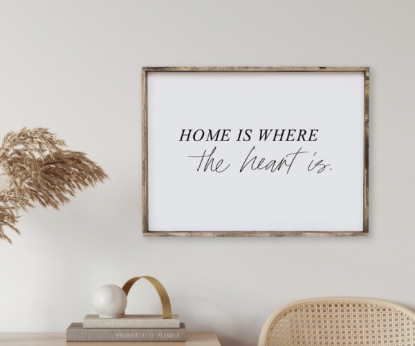Framed quote saying "Home is where the heart is" on a wall. Chair, books, and decorative reed vase are nearby.