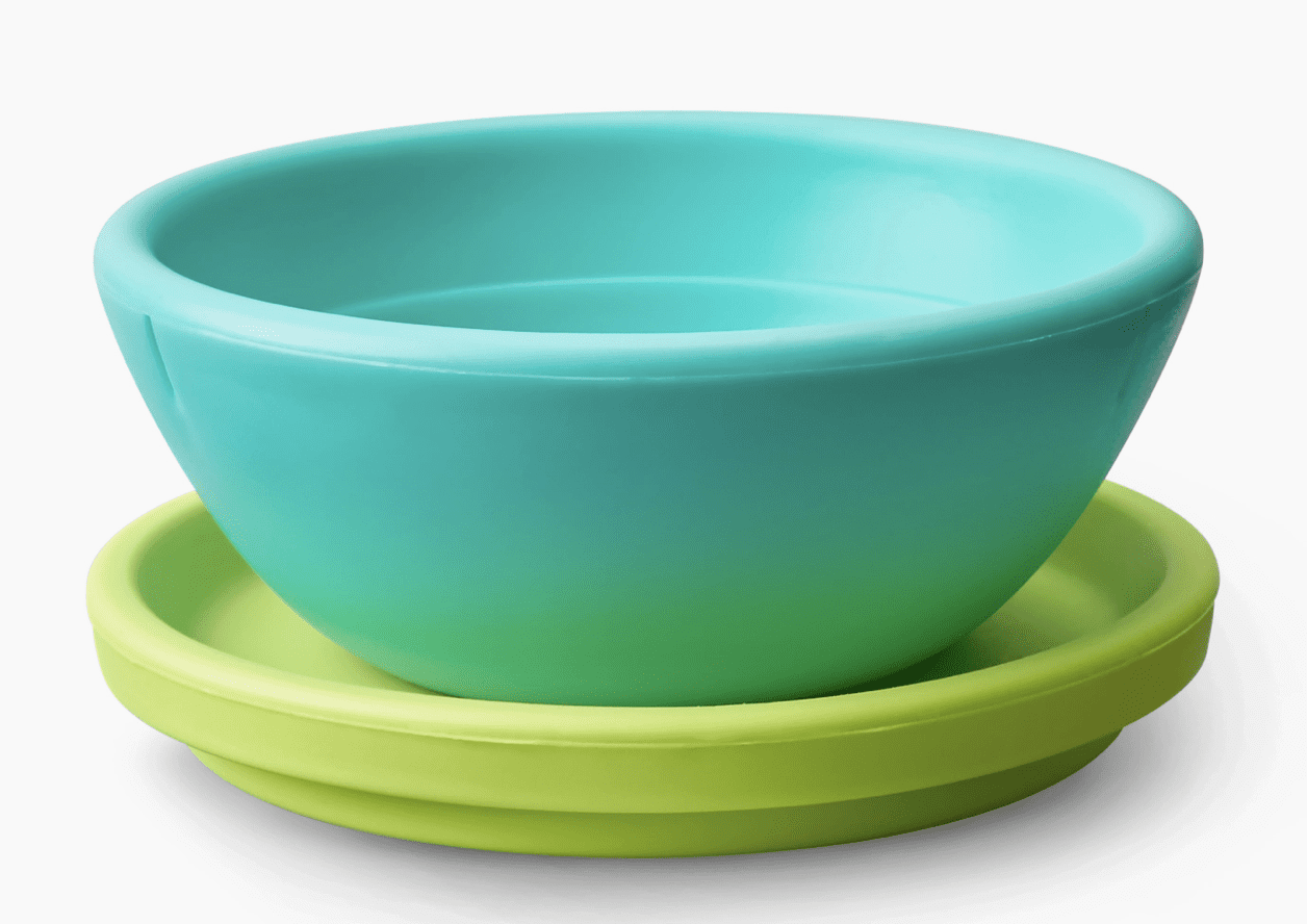 A light blue bowl sits atop a green saucer on a white background.