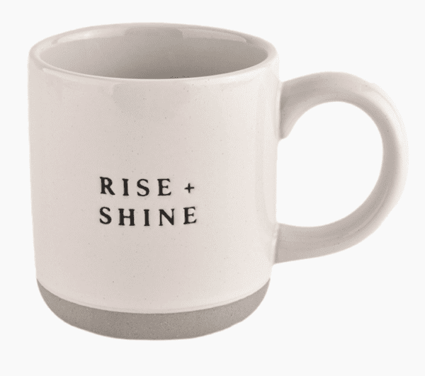 White mug with the words "RISE + SHINE" printed in black on the side.