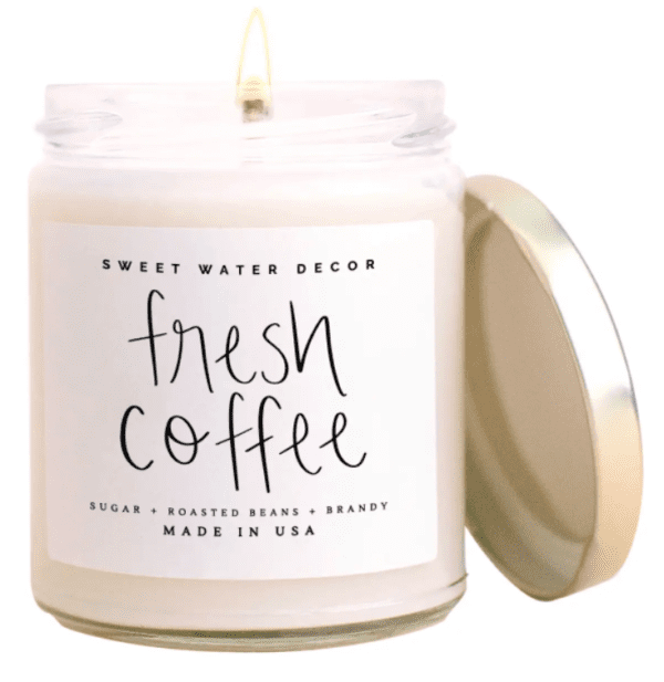 A lit candle in a clear jar with a gold lid. The label reads "Sweet Water Decor, fresh coffee, sugar, roasted beans, brandy, Made in USA.