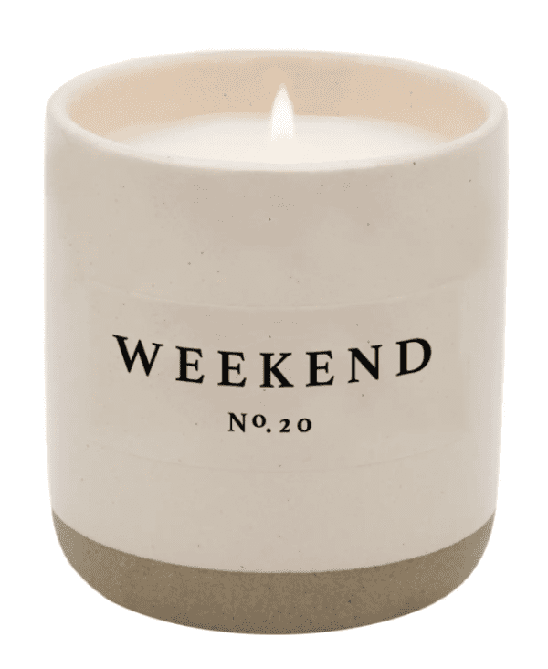 A lit white candle in a beige ceramic container labeled "Weekend No. 20.