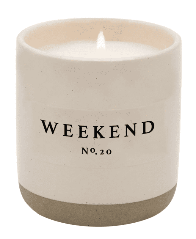 A lit white candle in a beige ceramic container labeled "Weekend No. 20.