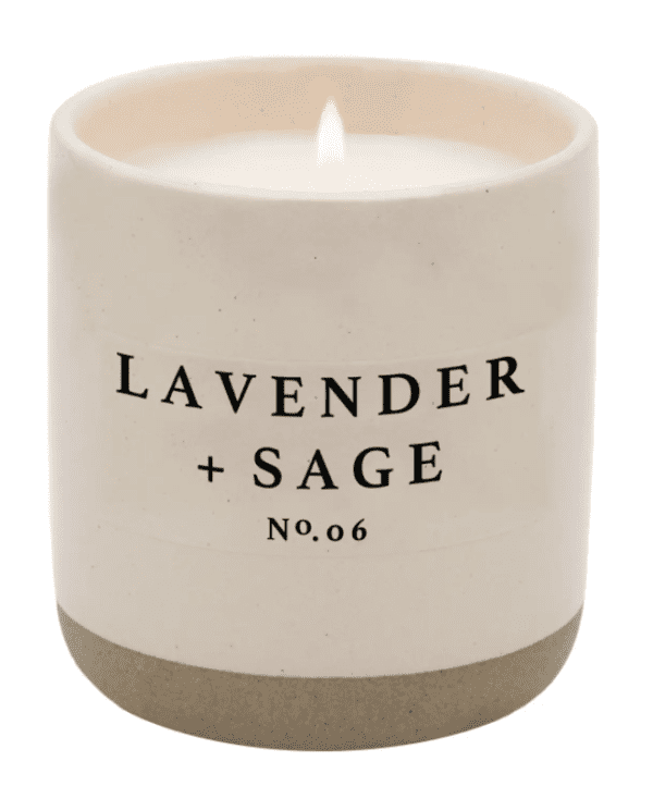 White candle with "Lavender + Sage No. 06" text on the front, lit and placed in a simple ceramic holder.