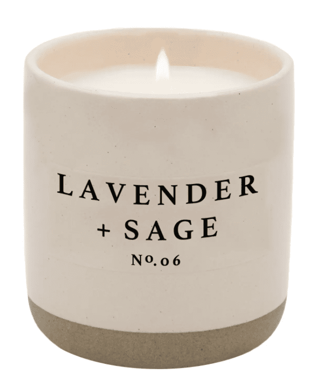 White candle with "Lavender + Sage No. 06" text on the front, lit and placed in a simple ceramic holder.