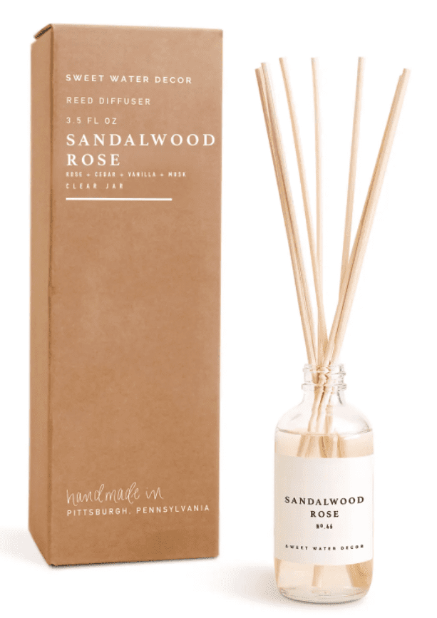 Reed diffuser with sandalwood rose scent in a glass jar beside a brown box labeled "Sandalwood Rose.