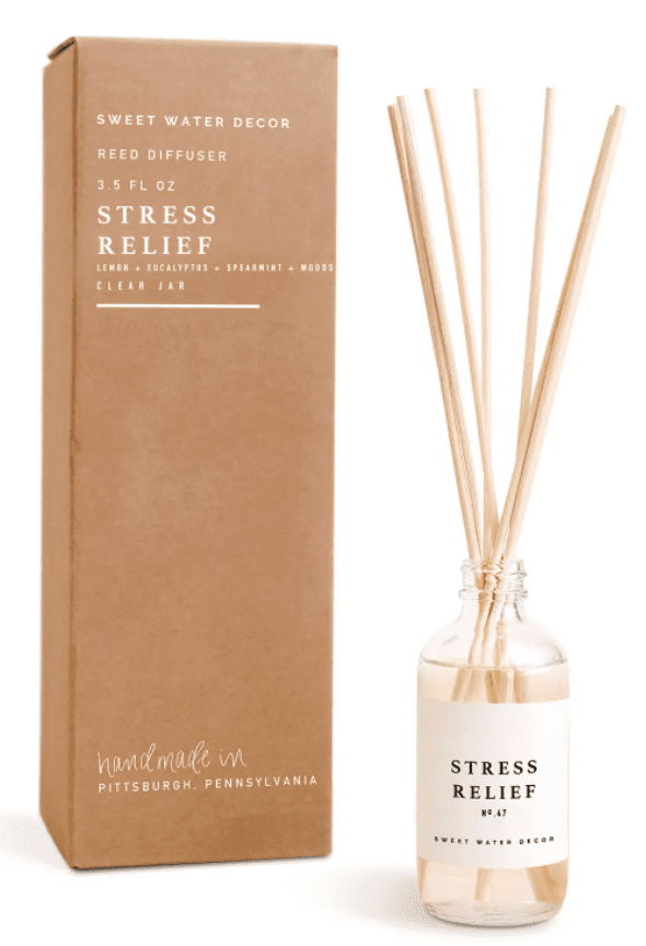 Reed diffuser labeled "Stress Relief" next to a brown box. The bottle contains reeds and is marked with fragrance details.