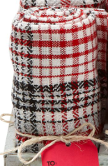 Stacked rolled textiles with red, black, and white plaid and star patterns, tied with twine on a gray surface.