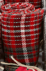 A stack of rolled woolen blankets with a red, black, and white plaid pattern.