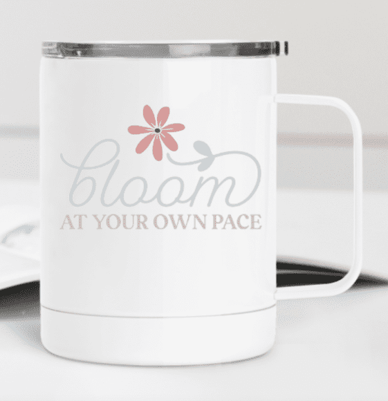 White mug with a floral design and the phrase "bloom at your own pace" printed on it.