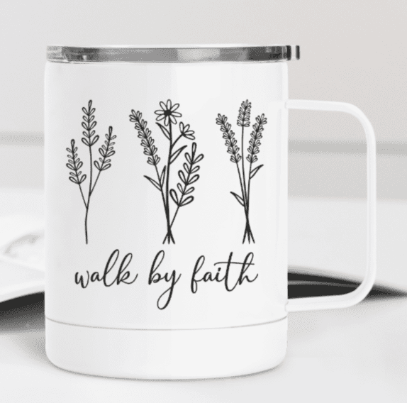 A white mug with black line drawings of flowers and the phrase "walk by faith.