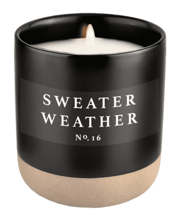 A lit candle in a black jar labeled "Sweater Weather No. 16" with a beige base.