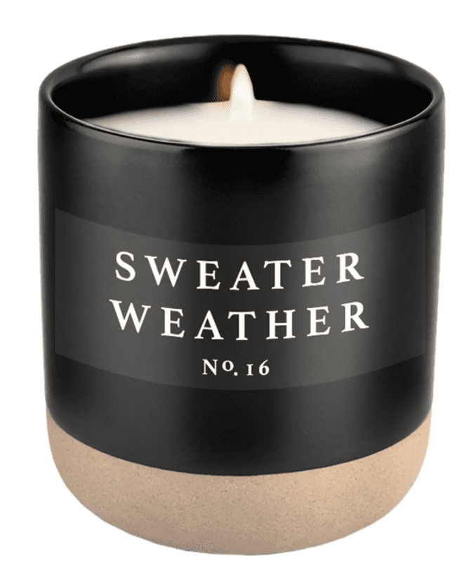 A lit candle in a black jar labeled "Sweater Weather No. 16" with a beige base.