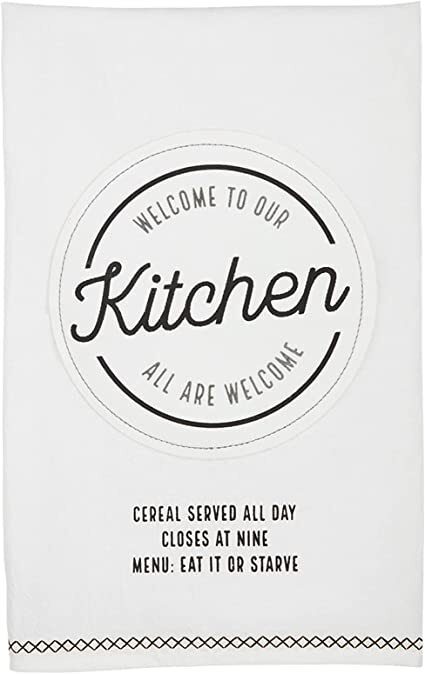 A white kitchen towel with text: "Welcome to Our Kitchen. All Are Welcome. Cereal Served All Day. Closes at Nine. Menu: Eat It or Starve.