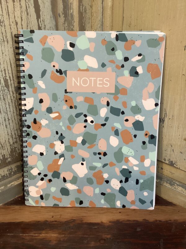 A spiral-bound notebook with a colorful abstract pattern cover and the word "NOTES" printed in a rectangular box.