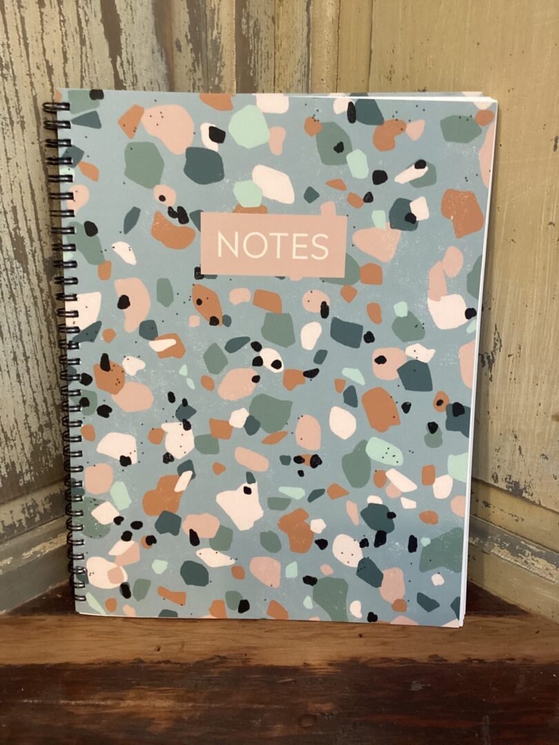 A spiral-bound notebook with a colorful abstract pattern cover and the word "NOTES" printed in a rectangular box.