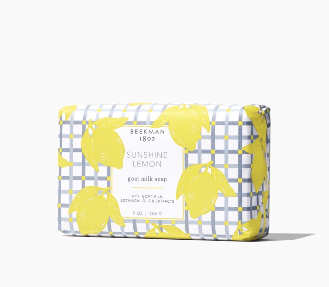 Rectangular bar of Beekman 1802 Sunshine Lemon goat milk soap, wrapped in lemon-patterned paper with a plaid background.