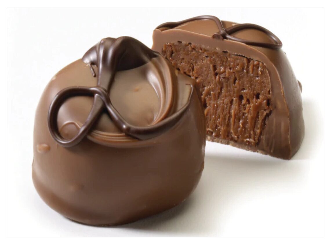 Two chocolate truffles, one whole and one cut open to show the textured filling, with decorative chocolate swirls on top.