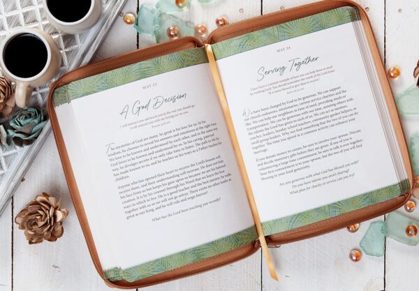 On a white wooden surface lies the open "Strength For Today For Couples (Ziparound Devotional)," displaying pages titled "A God Occasion" and "Serving Together," accompanied by two cups of coffee, decorative flowers, and pearls.