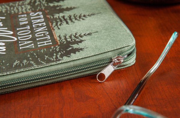 A green zippered pouch featuring a forest design and the phrase "Strength for Today," associated with the Strength For Today Men’s Devotional, is placed on a wooden surface next to a pair of eyeglasses.
