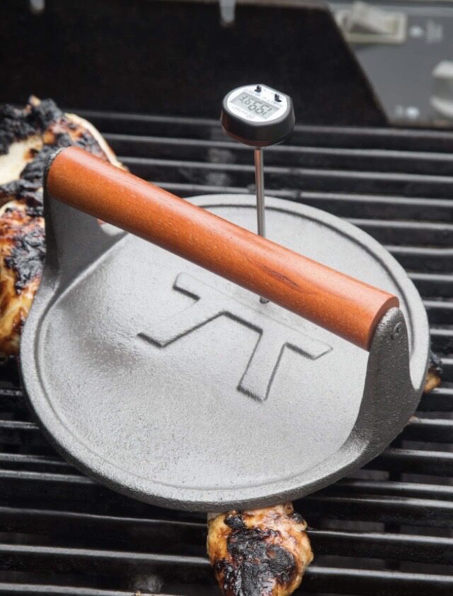 Cast iron grill press with thermometer on grill.