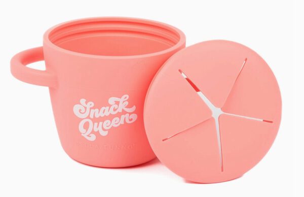 The Snack Queen Snacker is a pink silicone snack cup with its lid partially detached, revealing star-shaped slits for easy access.