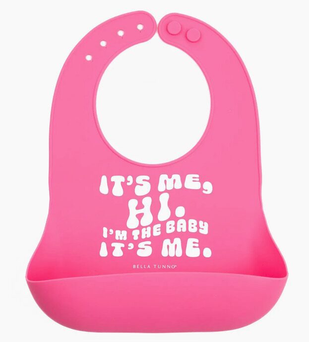 A pink silicone bib with white text that reads, "IT'S ME, HI. I'M THE BABY IT'S ME.