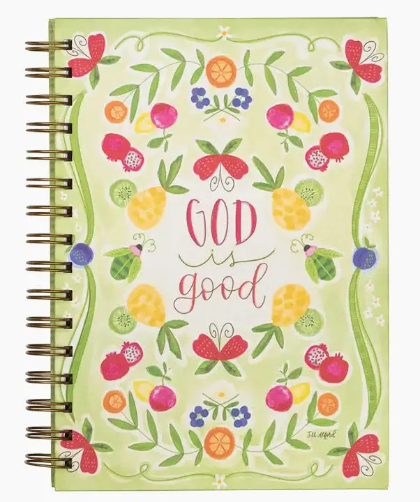 Spiral notebook with a floral and fruit design on the cover, displaying the text "God is good" in the center.