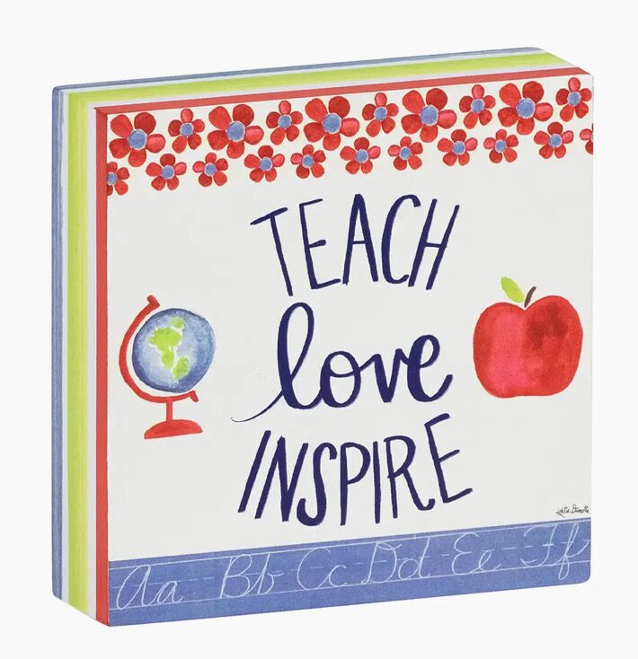 A decorative block with the phrases "Teach," "Love," and "Inspire" surrounded by red flowers, a globe, and an apple. The bottom edge shows letters A to Z in cursive.