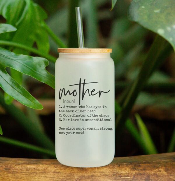 Glass jar with bamboo lid and straw, featuring the word "mother" and humorous definitions, surrounded by greenery.